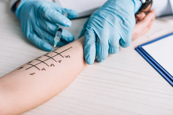 Allergologe mit Latexhandschuhen hält Spritze in der Nähe von Frau in Klinik — Stockfoto