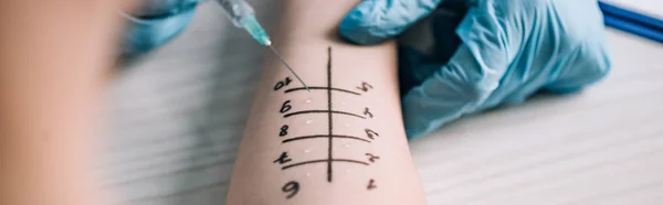 Panoramic shot of allergist in latex gloves holding syringe near woman while doing allergy test in clinic — Stock Photo