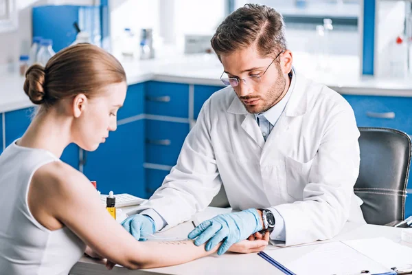 Selektiver Fokus des gut aussehenden Allergologen, der Lineal in der Nähe der markierten Hand der Frau hält — Stockfoto