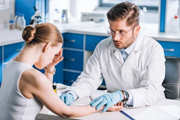 Selective focus of handsome allergist holding ruler near marked hand of sad woman — Stock Photo