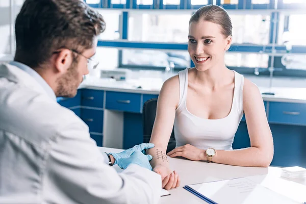 Selective focus of happy woman smiling near allergist with syringe — Stock Photo