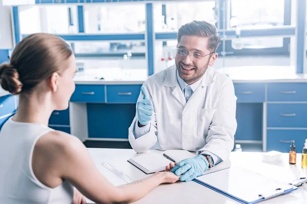 Enfoque selectivo de médico feliz mostrando el pulgar hacia arriba y la mano de la mujer en la clínica - foto de stock