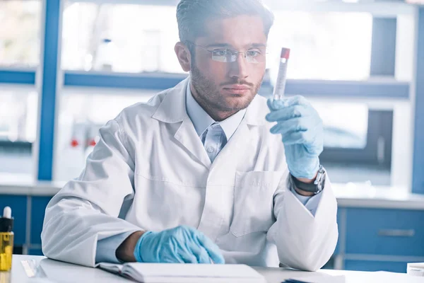 Handsome bearded immunologist in glasses looking at test tube — Stock Photo