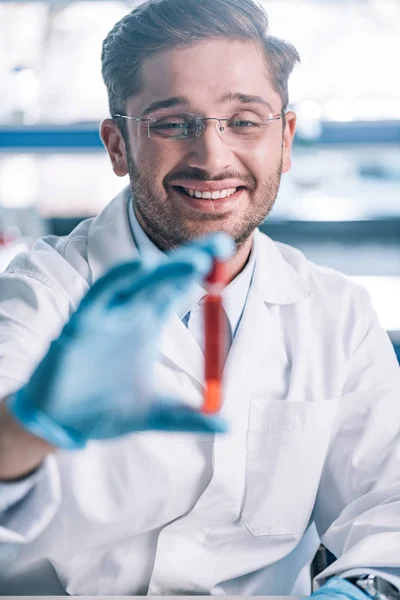 Foco seletivo de imunologista feliz segurando tubo de teste com líquido vermelho — Fotografia de Stock