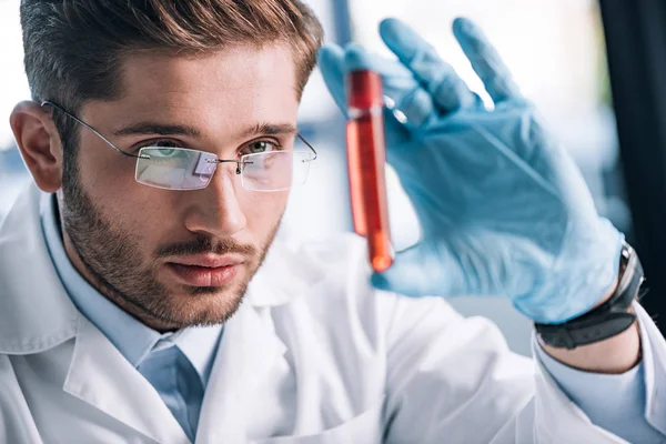 Enfoque selectivo del inmunólogo barbudo en gafas que sostienen tubo de ensayo con líquido rojo - foto de stock