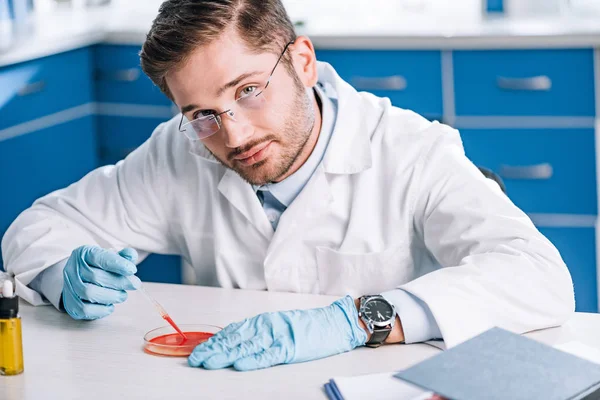 Handsome immunologist holding pipette with red liquid in lab — Stock Photo