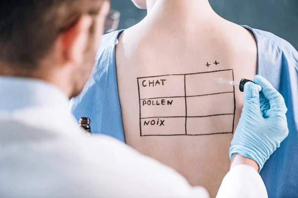 Selective focus of allergist holding pipette near woman with letters on marked body — Stock Photo