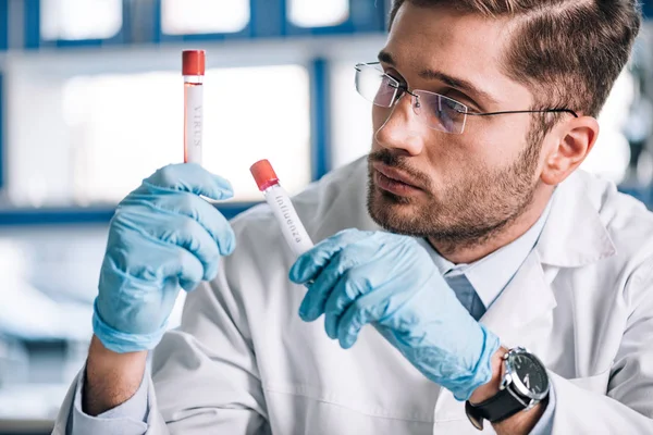 Selective focus of bearded immunologist looking at test tubes with letters — Stock Photo