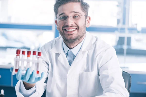 Selective focus of happy immunologist in glasses holding test tubes — Stock Photo