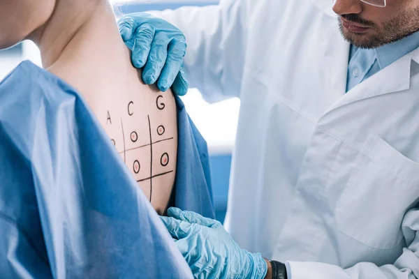Cropped view of allergist touching marked back with numbers and letters — Stock Photo