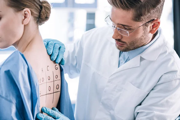 Alergista guapo de pie cerca de la mujer y tocando marcado de nuevo con números y letras - foto de stock