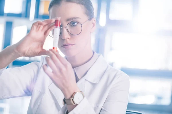 Selective focus of beautiful immunologist in glasses holding test tube — Stock Photo