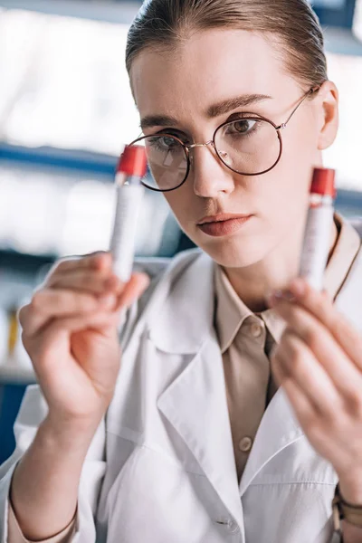 Selective focus of beautiful immunologist in glasses looking at test tubes — Stock Photo