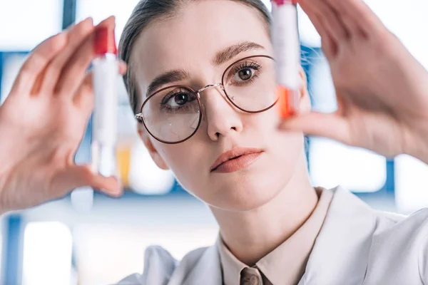 Enfoque selectivo del inmunólogo atractivo en gafas que miran los tubos de ensayo - foto de stock