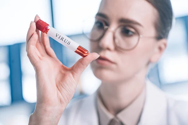 Selektiver Fokus des Immunologen in der Brille beim Blick auf das Reagenzglas mit Virenbuchstaben — Stockfoto