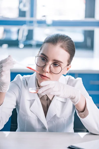 Selective focus of beautiful immunologist holding pipette with red liquid in laboratory — Stock Photo