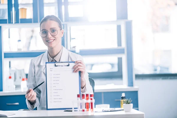 Atractivo y feliz inmunólogo portapapeles con lista de verificación y pluma - foto de stock