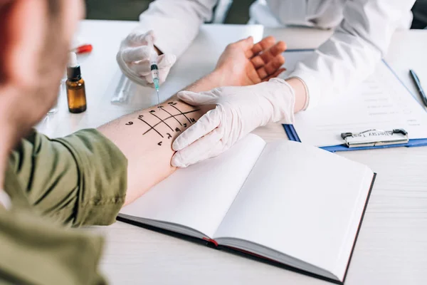 Cropped view of allergist holding syringe near man with marked hand — Stock Photo