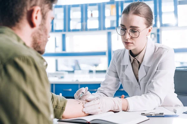 Selektiver Fokus attraktiver Allergologe hält Spritze in der Nähe von Mann in Klinik — Stockfoto