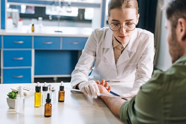 Selective focus of attractive allergist holding ruler near hand on man in clinic — Stock Photo