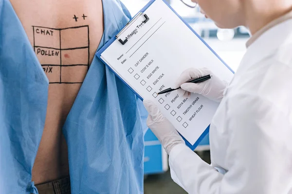 Vista cortada de alergista segurando caneta perto da lista de verificação enquanto segurando área de transferência perto do paciente — Fotografia de Stock