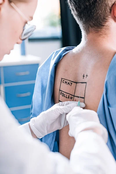 Cropped view of allergist in latex gloves holding syringe near man with marked back — Stock Photo