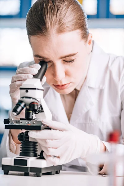 Selective focus of immunologist in latex gloves looking through microscope — Stock Photo