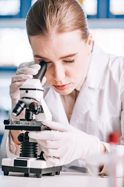 Enfoque selectivo del inmunólogo en guantes de látex mirando a través del microscopio - foto de stock