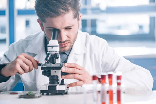 Selective focus of bearded biochemist looking through microscope in laboratory — Stock Photo