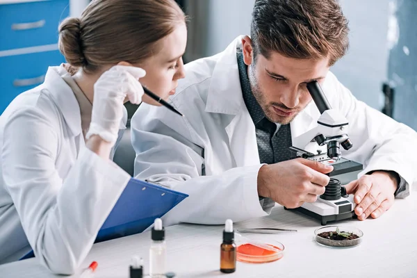 Attrayant biochimiste près de collègue regardant à travers le microscope — Photo de stock