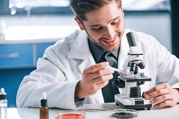 Selective focus of happy biochemist with pipette near microscope — Stock Photo