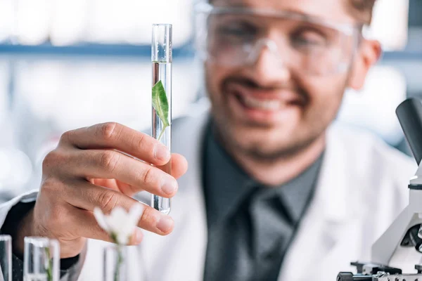 Enfoque selectivo de bioquímico feliz en gafas que sostienen tubo de ensayo de vidrio - foto de stock