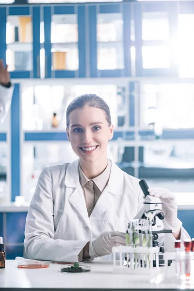 Foco seletivo do cientista feliz no casaco branco perto do microscópio — Fotografia de Stock