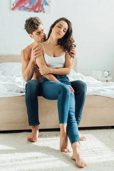 Мужчина без рубашки обнимает чувственную девушку, сидя на кровати — стоковое фото