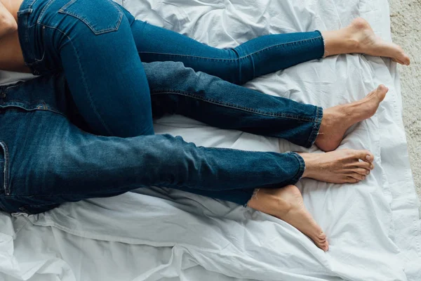 Cropped view of barefoot couple in denim jeans lying on bed — Stock Photo