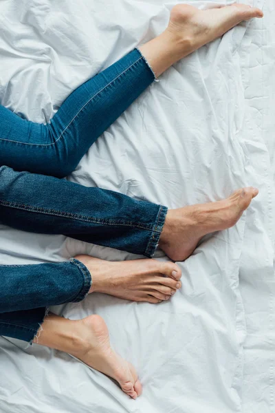 Частковий вид босоніж пара в джинсових джинсах лежить на ліжку — стокове фото