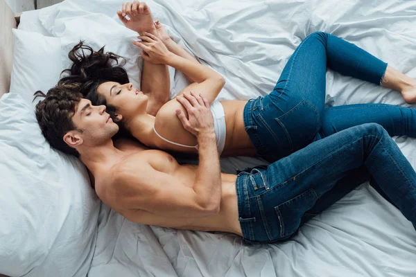 Top view of shirtless man embracing girlfriend while sleeping on bed together — Stock Photo