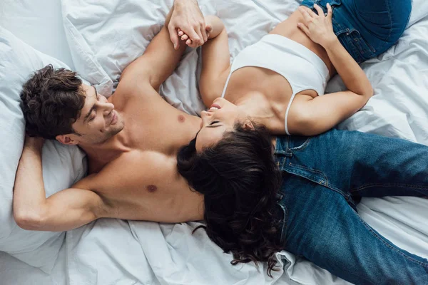 Top view of happy couple holding hands and looking at each other while lying on bed — Stock Photo