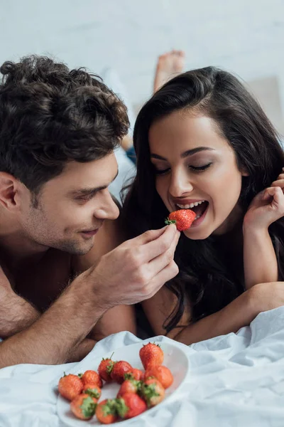 Handsome man feeding attractive girlfriend with strawberry — Stock Photo