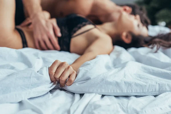 Foco seletivo na mulher em lingerie preta deitada na cama enquanto namorado abraçando-a — Fotografia de Stock