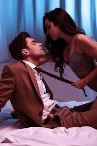 Сексуальная девушка в нижнем белье трогательный галстук бизнесмена, сидящего на кровати с закрытыми глазами — стоковое фото