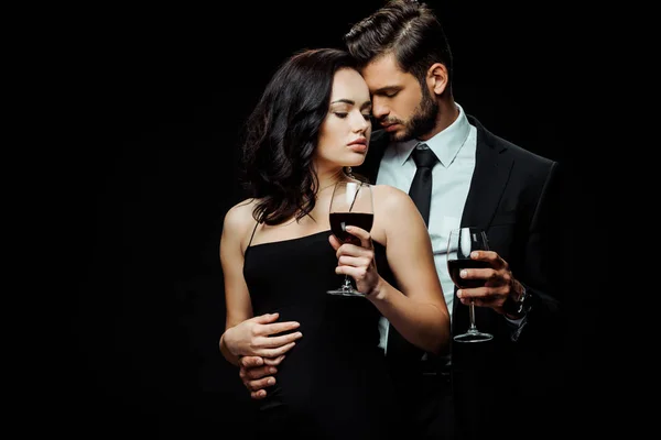 Handsome man and attractive woman holding glasses with red wine isolated on black — Stock Photo