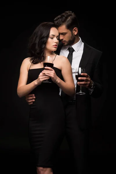 Bearded man and attractive girl holding glasses with red wine isolated on black — Stock Photo