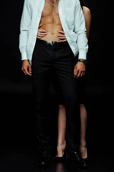 Обрезанный вид женщины, касающейся мускулистого мужчины в рубашке на черном — стоковое фото