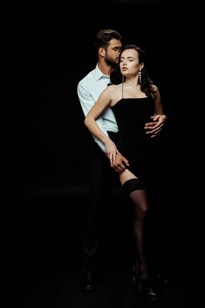 Homem apaixonado tocando mulher sexy no vestido isolado no preto — Fotografia de Stock