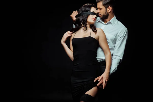 Leidenschaftlicher bärtiger Mann berührt Kleid seiner Freundin mit verbundenen Augen isoliert auf schwarz — Stockfoto
