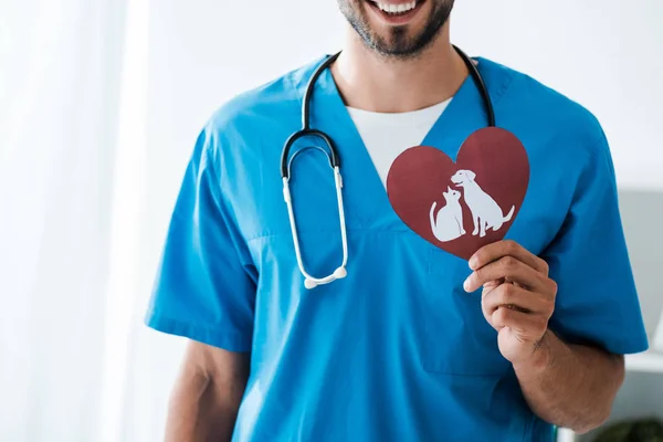 Cropped view of smiling veterinarian showing paper cut heart with dog and cat symbols — Stock Photo