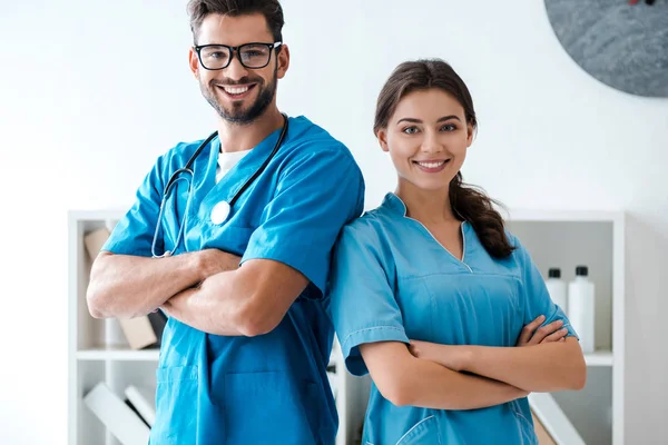 Dos jóvenes veterinarios confiados de pie con los brazos cruzados y sonriendo a la cámara - foto de stock