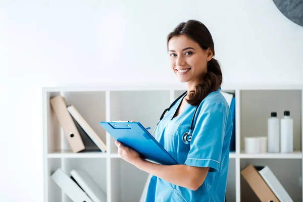 Hermoso veterinario sonriendo a la cámara mientras escribe prescripción en portapapeles - foto de stock