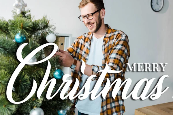 Happy bearded man in glasses decorating christmas tree in office with merry christmas illustration — Stock Photo